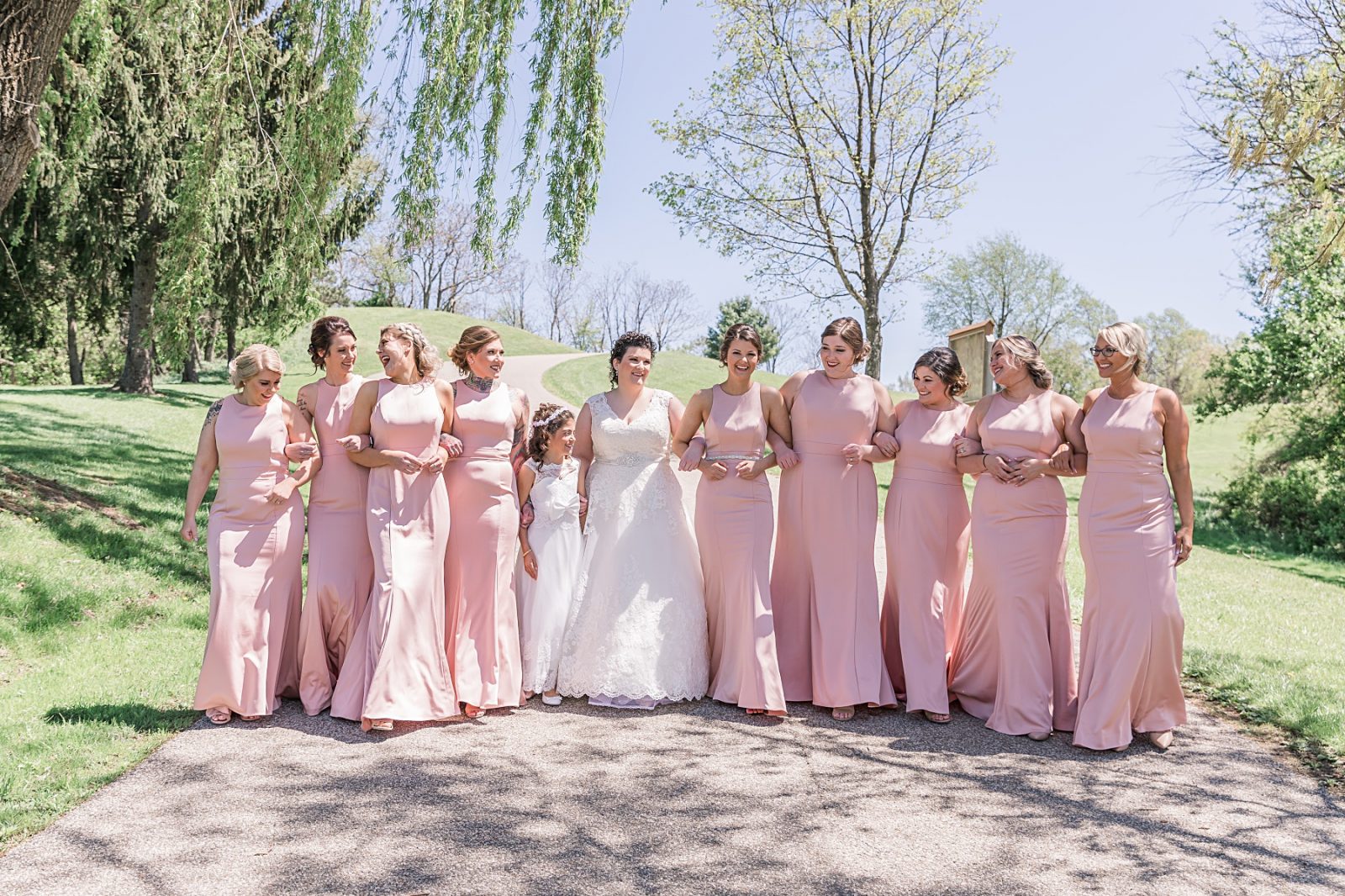 Wedding photography by Diana Gramlich, Bride with bridesmaids in blush Allure dresses walking on a road arms linked