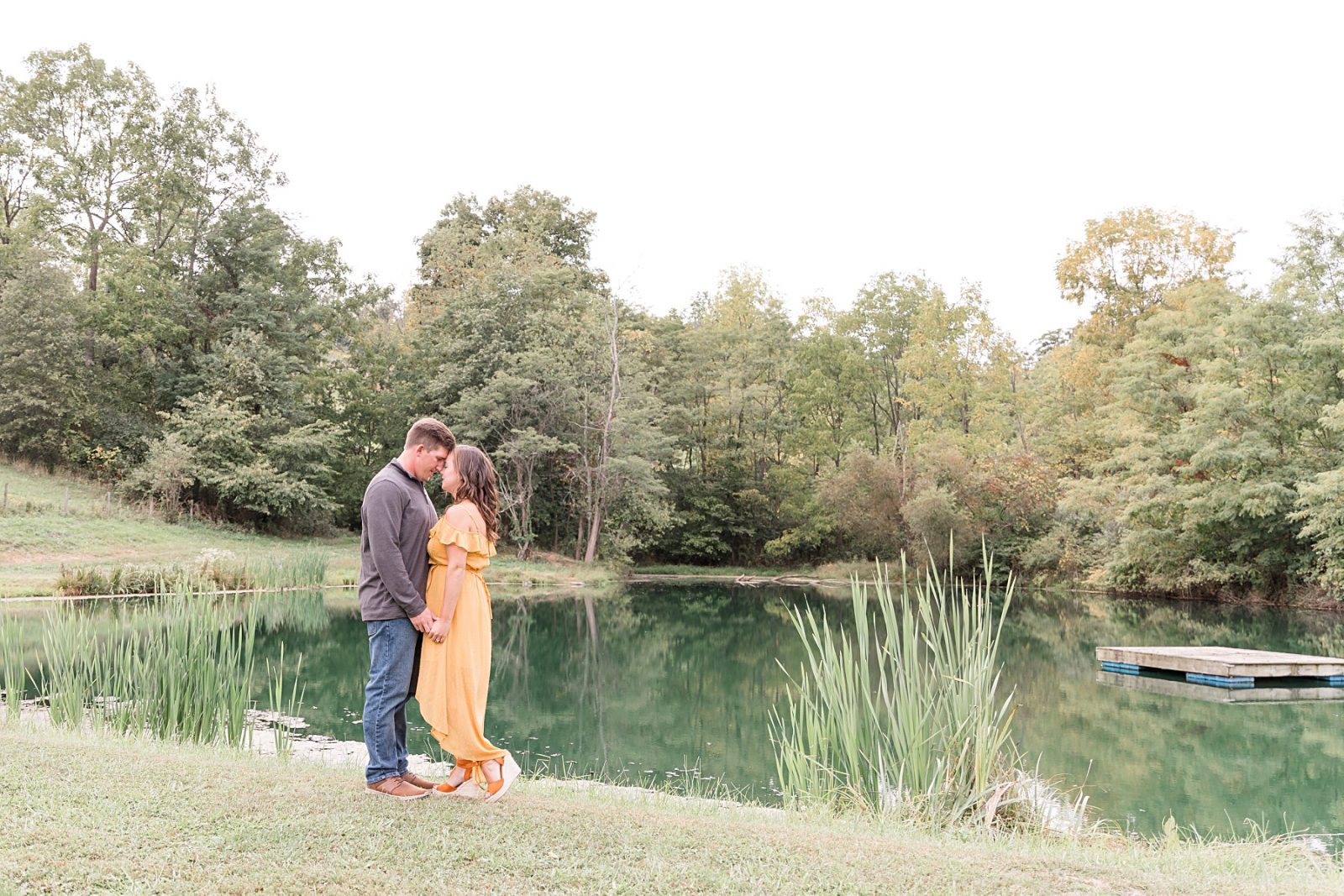 Engaged couple standing forehead to forehead in front of a pond