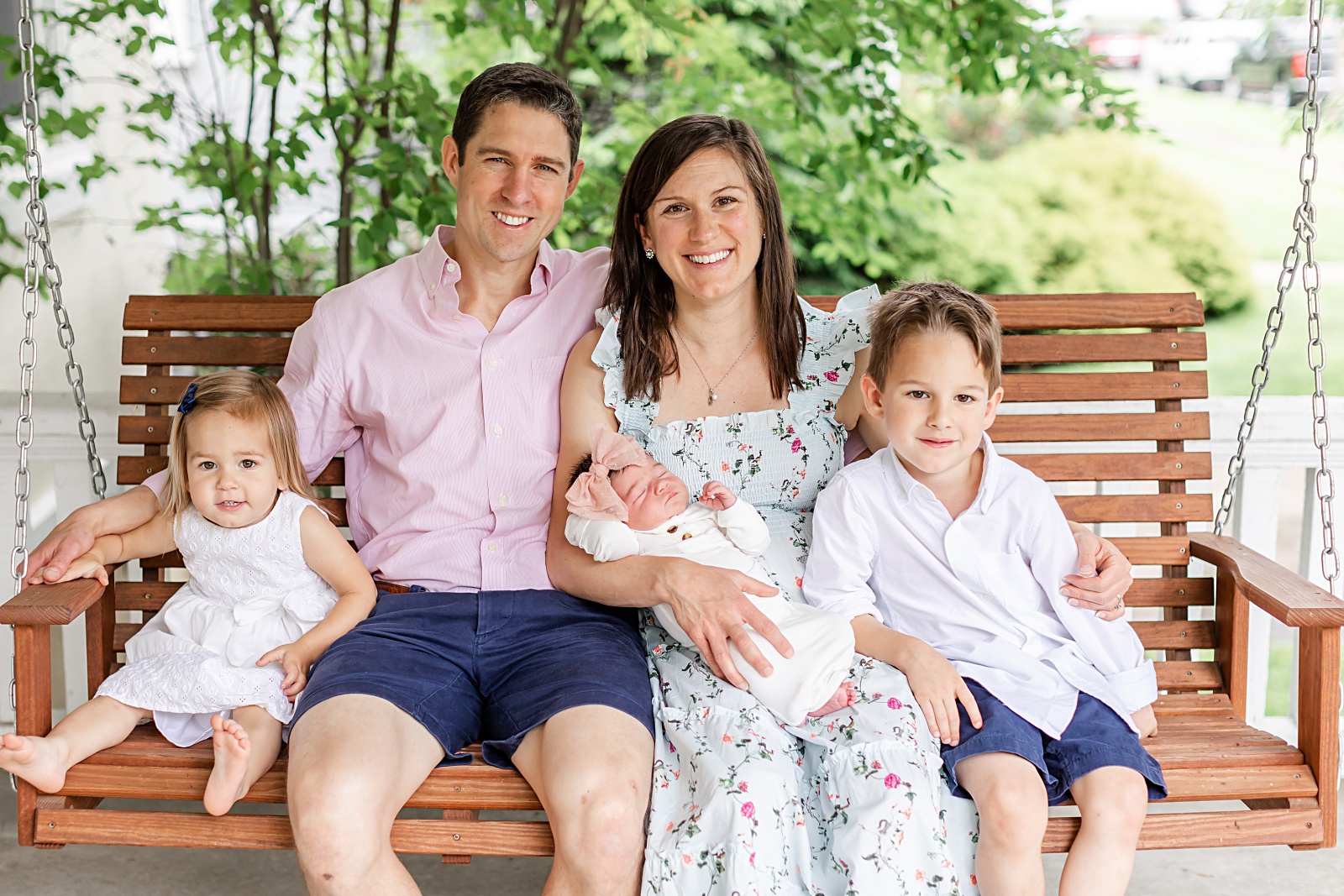 Mom, Dad and three children sitting on a porch swing smiling at the camera