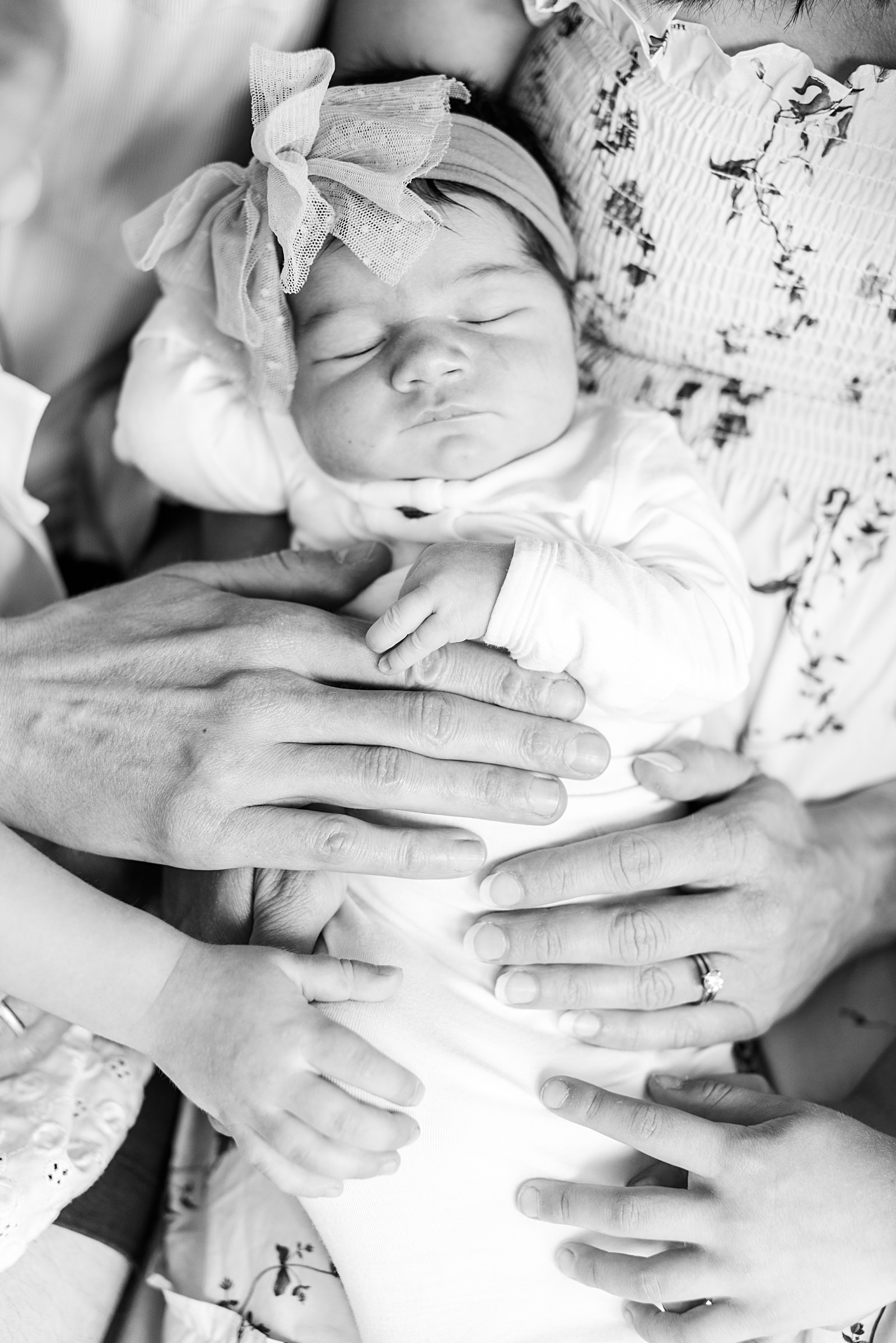 a newborn baby is sleeping in moms arms while dad and 2 siblings have their hands on baby 