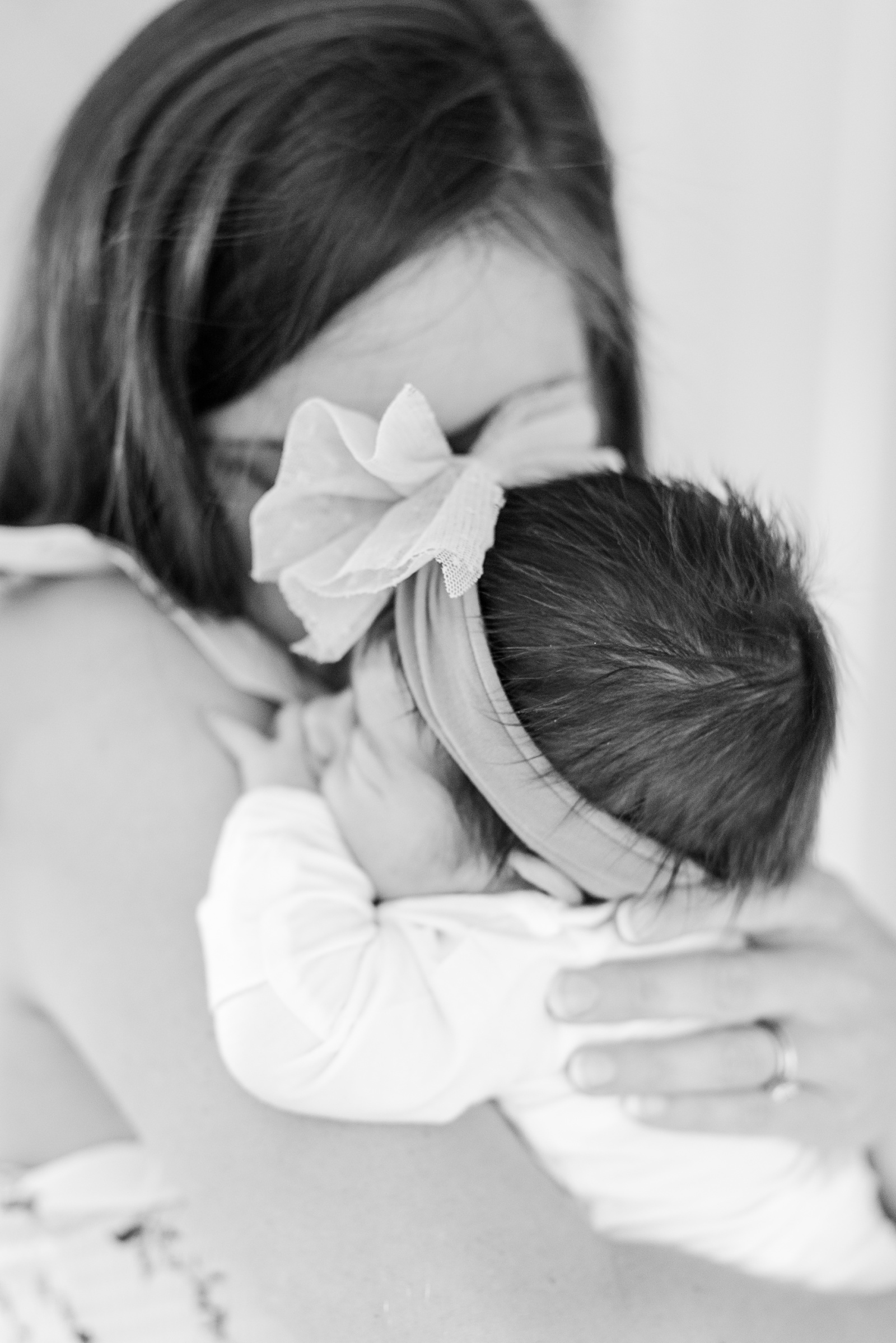 mom is holding a sleeping newborn baby girl and kissing her on a cheek