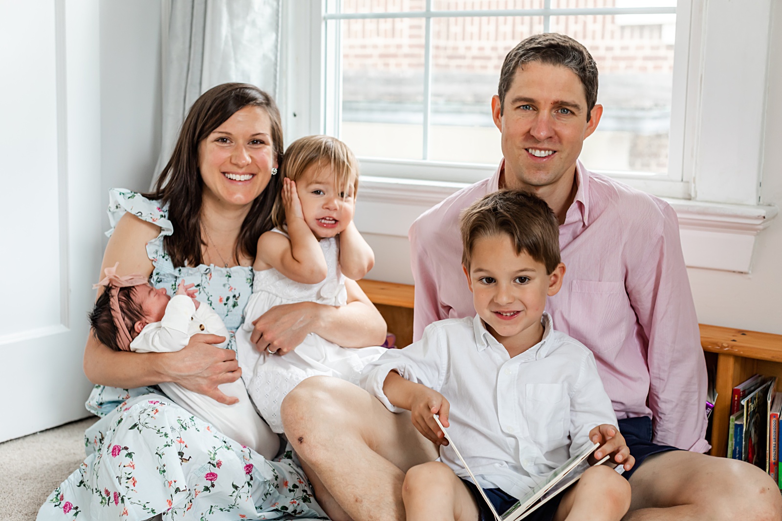 a family of five are sitting on the floor in the nursery smiling at the camera